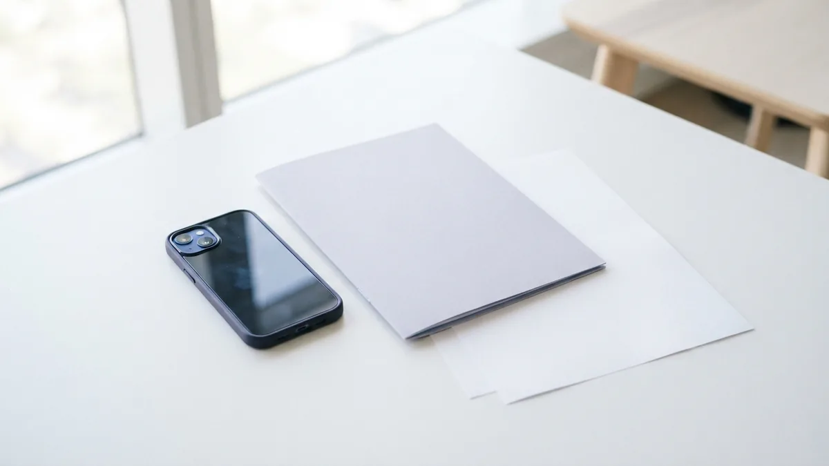Phone and folder on a white surface Smartphone beside a folder and blank sheets, representing PDF downloads on a device